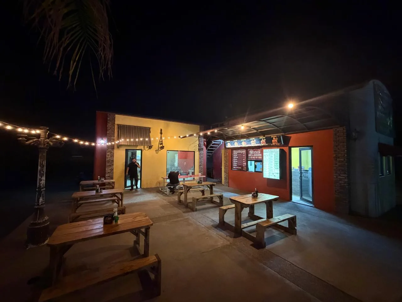 Patio nocturno de Desert Roll & Burguers con mesas de pino y luces cálidas